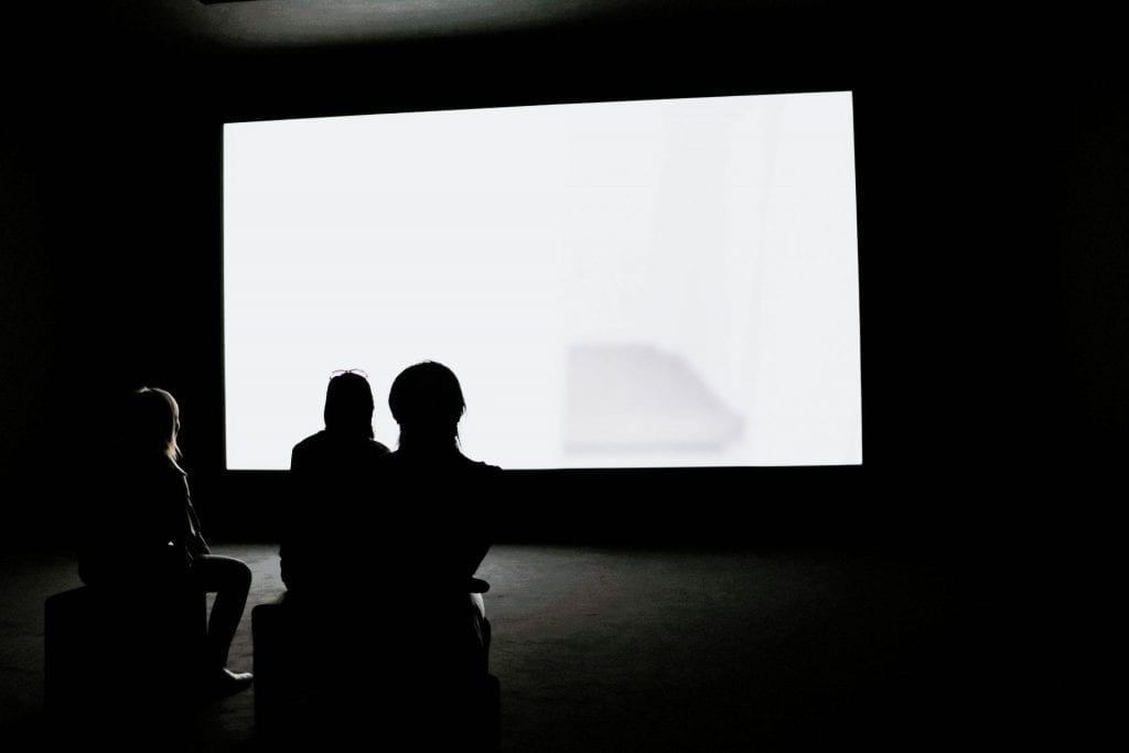 The silhouette of three people watching a blank movie screen.