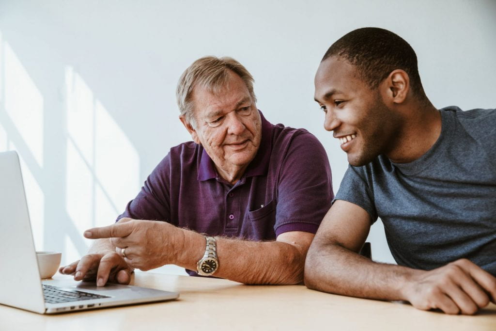 A white man points at a laptop and a black man smiles while looking at the laptop.